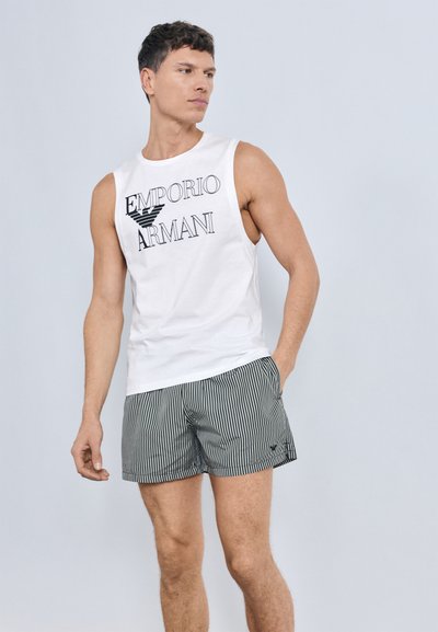 White sleeveless shirt with "Emporio Armani" logo in black; paired with green and white striped shorts, featuring a relaxed fit and lightweight fabric.