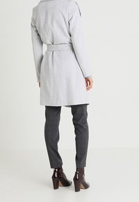 Ljusgrått ullrock med bälte, långa ärmar och strukturerad krage; tillsammans med grå rutiga byxor och blanka bordeauxfärgade klackstövlar.