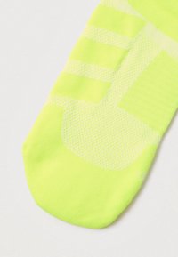 Calcetín amarillo neón con patrones de malla texturizados, puntera sin costuras y detalles acanalados. Tejido flexible para mayor comodidad y transpirabilidad.