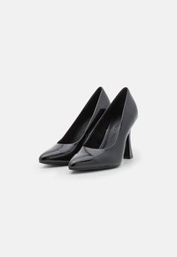 Zapatos de charol negro de tacón alto con punta afilada y tacón grueso, que presentan una textura suave y un diseño minimalista.