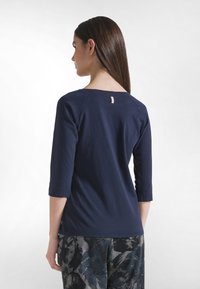 Granatowy, lekki bawełniany top z rękawami do połowy łokcia, szerokim dekoltem i małą metką z tyłu, w połączeniu ze spodniami w wzory.