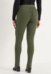 Groene skinny jeans met een gladde textuur, voorzien van achterzakken en een hoge tailleband, gecombineerd met zwarte haklaarzen.