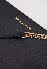 Černá kožená kabelka s texturovaným povrchem, zdobená zlatým řetízkem a vyraženým logem "MICHAEL KORS" ve zlatém písmu.