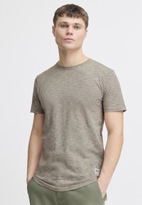 Olivengrøn t-shirt i et tekstureret, blødt stof med rund hals, korte ærmer og logo-patch i kanten. Har et subtilt stribemønster.
