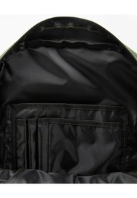 Groene rugzakinterieur, met een zwarte, gladde voering en meerdere vakken voor organisatie en een ritssluiting.