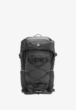 Black Volcom backpack with top flap, front zip pocket, adjustable straps, elastic cords, and side zippers, shown against a white background.
