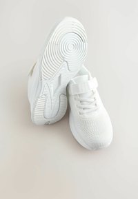 Baskets athlétiques blanches avec un dessus en mesh texturé, un bout arrondi et une sangle en Velcro. La semelle présente des motifs de semelle circulaires pour une meilleure adhérence.