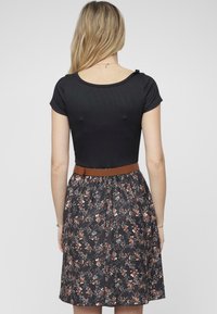 Haut noir à manches courtes et décolleté arrondi, associé à une jupe à motif floral dans des tons sombres, cintrée à la taille avec une ceinture marron.
