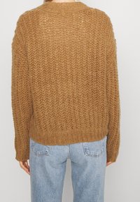 Brauner, gestrickter Pullover mit lockerer Passform, der ein strukturiertes Muster und einen gerippten Saum aufweist. Die Rückansicht zeigt weiches Garn und einen runden Halsausschnitt.