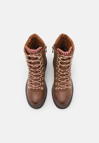 Hnědé kožené turistické boty se zlatými kovovými očky, pruhovanou červenou a bílou podšívkou a texturovanou podrážkou. Obsahují tkaničky a boční zipy.