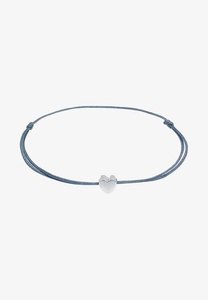 Egy ezüst szívmedál vékony kék zsinóron, állítható csomózási megoldással a személyre szabott illeszkedéshez. Simább felület és egyszerű dizájn.