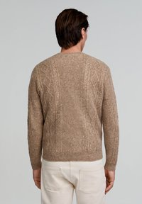 Beżowy sweter z dzianiny w warkocze z okrągłym dekoltem, ściągaczami przy mankietach i u dołu; ma teksturowany wzór na plecach i rękawach.