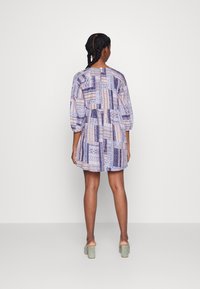 Vestido curto e estampado com tons de azul, creme e marinho, com um corte solto, mangas longas e um design em camadas. Calçado é uma sandália de salto bloco.