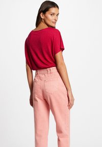 Rode, glanzende top met korte mouwen, gecombineerd met hoge taille, lichtroze denim broek; gladde textuur en standaard achterzakken zichtbaar.