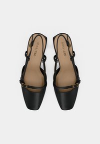 Chaussures à bride arrière noires avec un bout carré, une texture en cuir lisse, des fines brides et un accent de boucle dorée. L'intérieur comprend une semelle beige rembourrée.