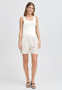 Vit ärmlös topp kombinerad med beige veckade shorts. Sandaler med svarta remmar. Lätt tyg och avslappnad passform. Neutral färgpalett.