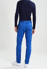 Modré bavlněné kalhoty s úzkým střihem, plochými kapsami a hladkým povrchem. Nosit s námořnickým topem s dlouhým rukávem a bílými teniskami.