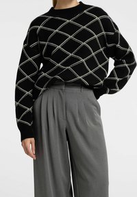 Svart stickad tröja med vitt diamantmönster, ribbat halsband och långa ärmar. Matchad med grå veckade byxor.