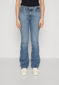 Jeans in denim azzurro chiaro con vestibilità dritta, dotati di cinque tasche, chiusura con zip e leggere sfumature sul tessuto. Abbinati a sneakers bianche.