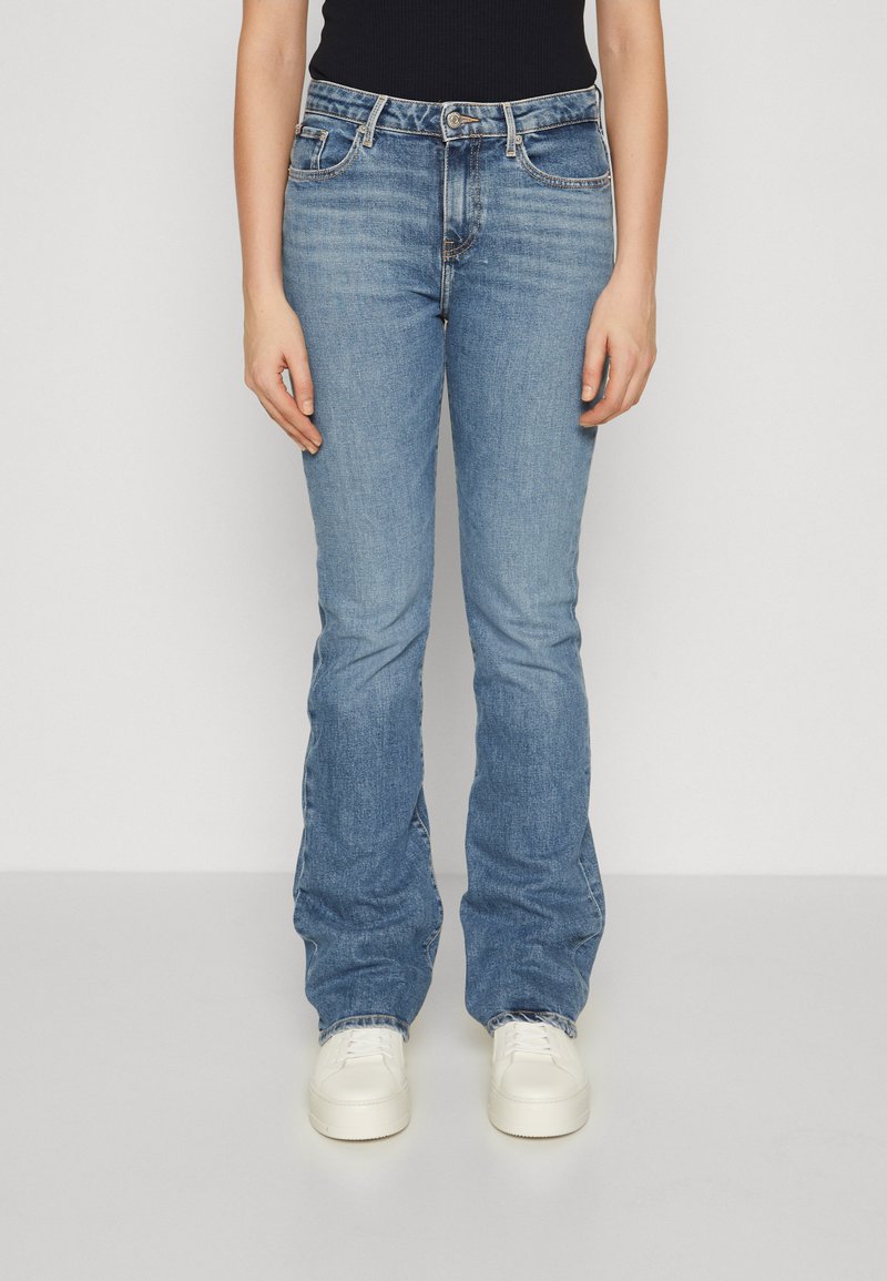 Jeans in denim azzurro chiaro con vestibilità dritta, dotati di cinque tasche, chiusura con zip e leggere sfumature sul tessuto. Abbinati a sneakers bianche.