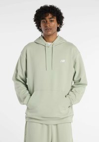 Felpa con cappuccio verde chiaro realizzata in tessuto morbido, con tasca a marsupio e un piccolo logo bianco sul petto. Vestibilità comoda.