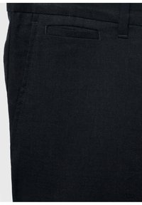 Țesătură închisa la culoare, albastru navy, în prim-plan, având pantaloni structurați, cu o curea frontală plată și o textură netedă, cu detalii țesute subtile.