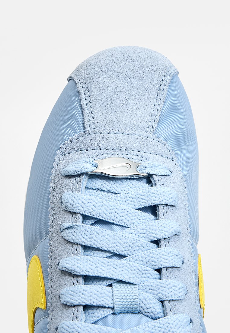 Baskets bleu clair avec une tige en daim et en synthétique, logo d'accent jaune, lacets plats et capuchon de talon texturé.