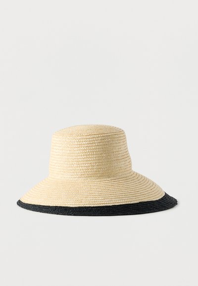 Ψάθινο καπέλο με πλατύ γείσο, σε φυσικό μπεζ χρώμα και αντίθετο μαύρο τελείωμα στο κάτω μέρος. Υφή υφασμένης πλέξης.