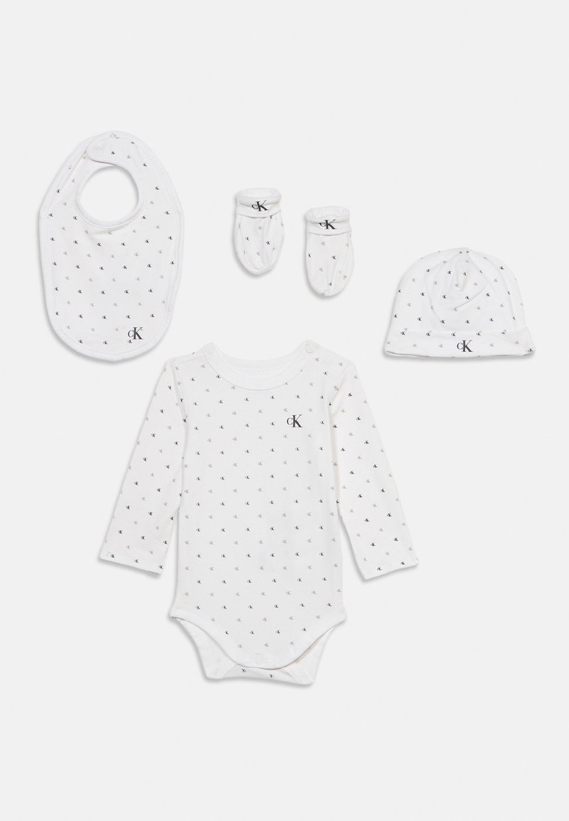 Σετ λευκά ρούχα μωρού με αμάνικο κορμάκι, γάντια, καπέλο και σαλιάρα, όλα με μικρά μαύρα λογότυπα "CK" και κουμπώματα.