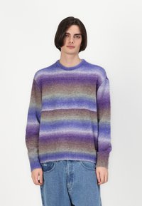 Paars en bruine gestreepte trui, gemaakt van een zachte brei stof, met een ronde hals en geribde boorden. Casual pasvorm, gedragen met denim.