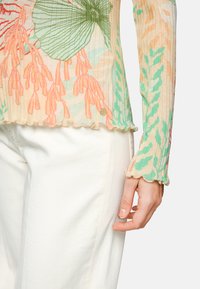 Langärmliges Oberteil mit geripptem Textil in floralen Mustern in Grün, Orange und Creme. Ausgefranster Saum und ein kleines Metallic-Logo-Detail.