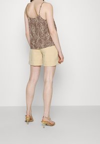Brązowy top w panterkę z cienkimi ramiączkami w połączeniu z beżowymi szortami z podwiniętymi mankietami. Złote sandały na obcasie dopełniają całość.