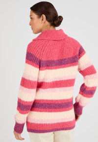 Maglione oversize a righe nei toni del rosa, crema e viola; texture a coste; ampio colletto; maniche lunghe; con righe spesse e sottili alternate.