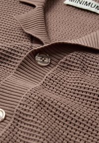 Cardigan en brown texturé avec un design côtelé, doté d'un bouton transparent et d'une étiquette portant la mention "MINIMUM". Tissu en tricot doux.
