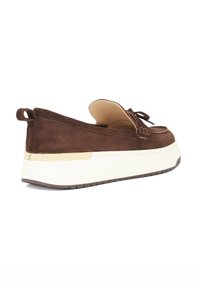 Brown suede slip-on shoe with a rounded toe, lace detailing, and a chunky white sole featuring a gold accent. Textured upper with a smooth lining.