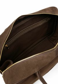 Brown suede handbag interior with a zip pocket, dual fabric lining, and golden zipper detailing. Soft texture and spacious design.