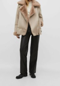 Beige faux shearling jacket with a wide collar, zip closure, and side pockets. Paired with black faux leather pants and chunky black boots.