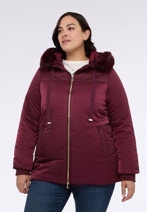 Giacca a vento borgogna con cappuccio foderato in pelliccia sintetica, chiusura con zip, due tasche laterali e polsini a costina. Tessuto liscio e leggero.