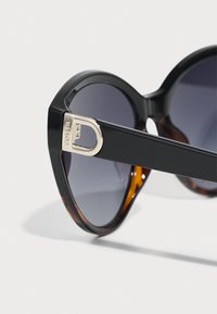 Occhiali da sole a gatto in nero e tartaruga con lenti sfumate, con un accento in hardware oro sul tempio.