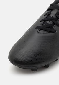 Scarpino da calcio nero con superficie testurizzata, caratterizzato da una punta curvata e un sistema di allacciatura centralizzato. La suola presenta numerosi tacchetti rotondi per una migliore trazione.