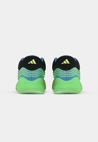 Sapatos atléticos em verde brilhante, azul e preto com um design ondulado no calcanhar e um logótipo triangular na parte de trás, vistos de trás sobre um fundo branco.