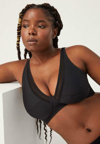 Bralette atlético negro con escote pronunciado, acentos de malla transparente y tirantes ajustables; tejido suave y elástico.