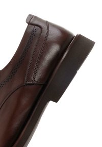 Zapato de cuero marrón con un diseño elegante, textura suave, detalles de costura sutiles y una suela de goma oscura y baja.