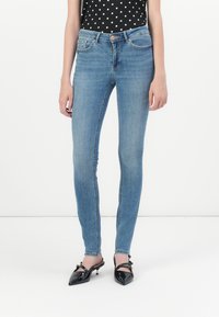 Slim-fit blue denim jeans with a five-pocket design, light wash, and subtle fading, paired with black polka dot top and black heeled shoes.