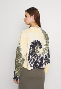 Felpa tie-dye gialla e verde con accenti scuri, caratterizzata da un design corto, maniche lunghe e una vestibilità rilassata. Tessuto texturizzato.