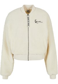 Giacca bomber color crema realizzata in materiale di pelliccia sintetica testurizzata, con polsini a coste e chiusura con zip. Presenta un ricamo del logo discreto sul petto.