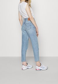 Ljusblå högmidjade jeans med rak benkjol, som har en beige läderlapp, klassiska bakfickor och synliga sömdetaljer.