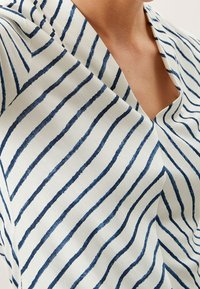 Blusa de algodón con escote en forma de V, con un fondo blanco y rayas horizontales en color marino. La tela tiene una textura suave.