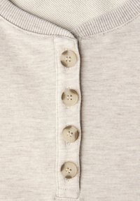 Jasnobeżowa koszulka henley z prążkowanym dekoltem, czterema plastikowymi guzikami z przodu i miękką, teksturowaną tkaniną.