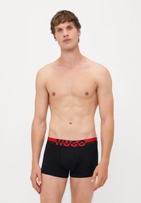 Schwarze Boxershorts mit rohem elastischem Bund, der das „HUGO“-Logo trägt. Glatte Stoffqualität, taillierte Passform und kurzes Bein-Design.